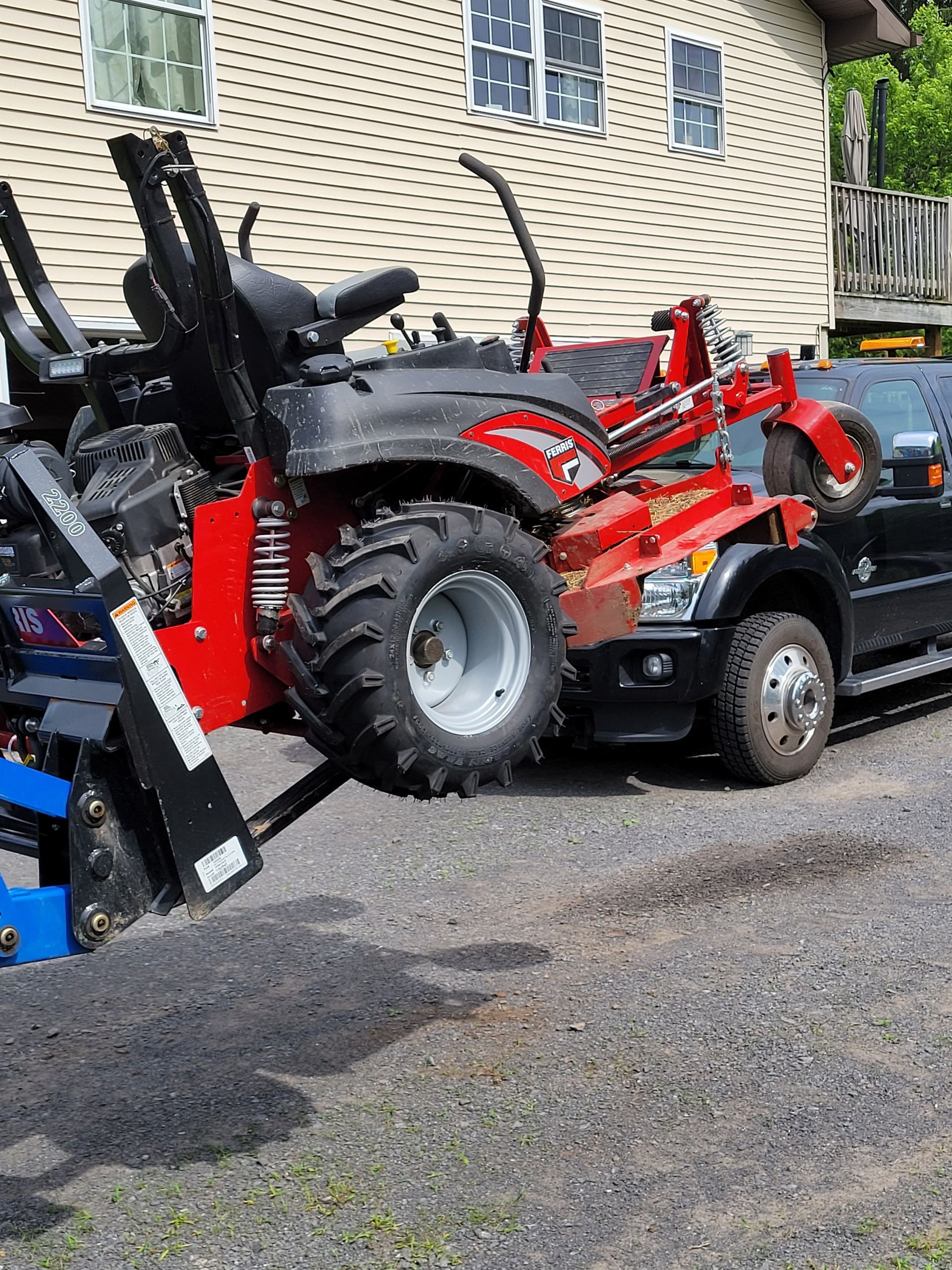 Red tractor being loaded onto a black truck bed on gravel.