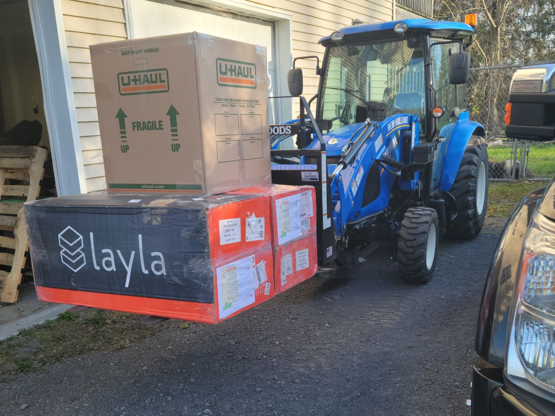 Blue tractor with boxes on front lift; driveway setting.