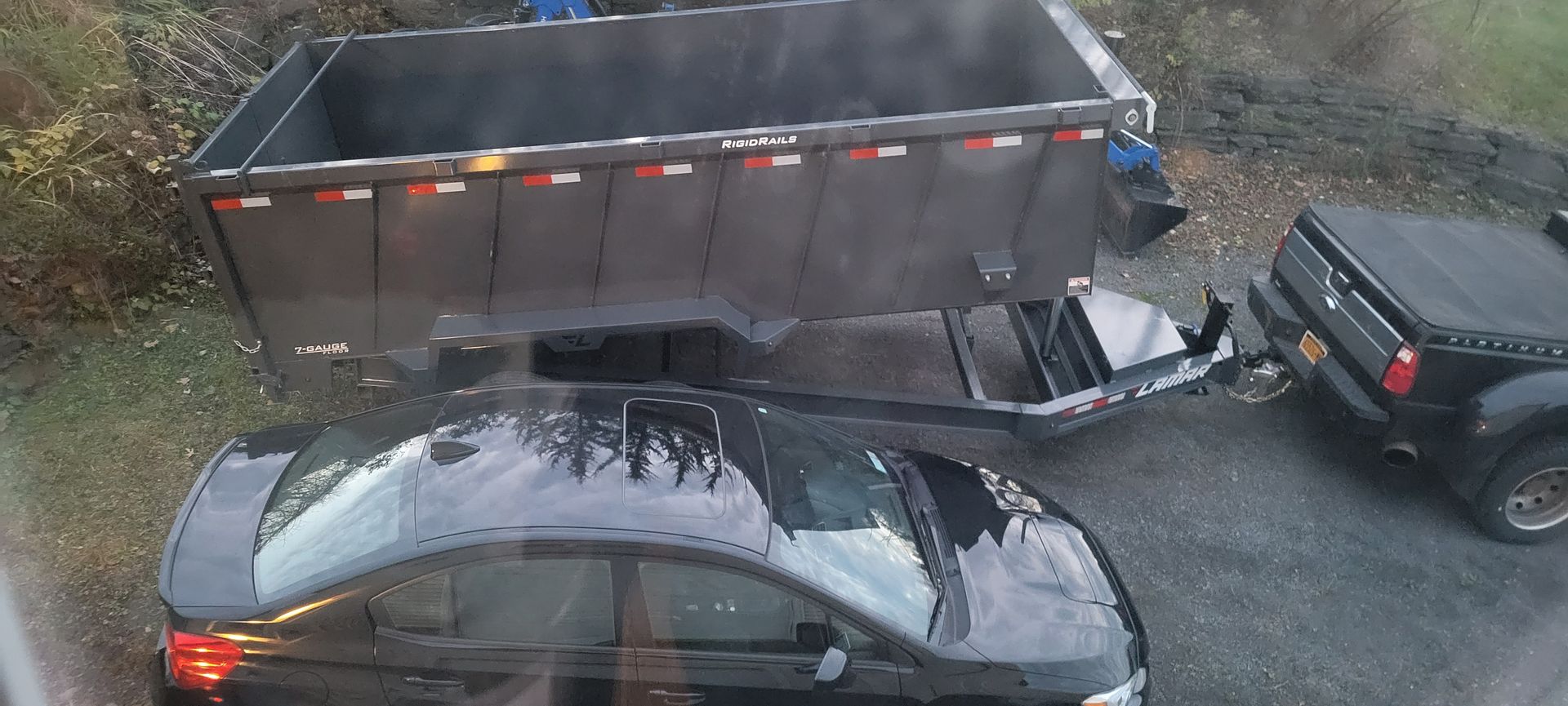 Black car next to a black truck hooked to a large dump trailer.