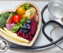 Heart-shaped bowl filled with fruits and vegetables beside a stethoscope