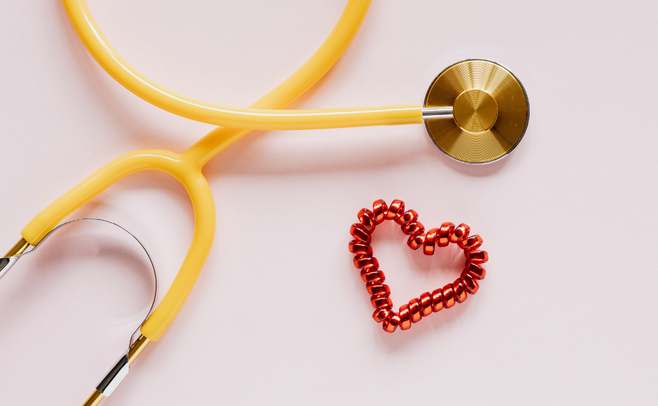 Yellow stethoscope next to a red heart made of beads on a light pink surface.