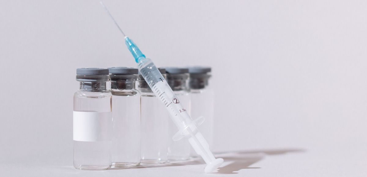 Peptide Syringe with blue needle cap leaning against clear  vials on a white surface