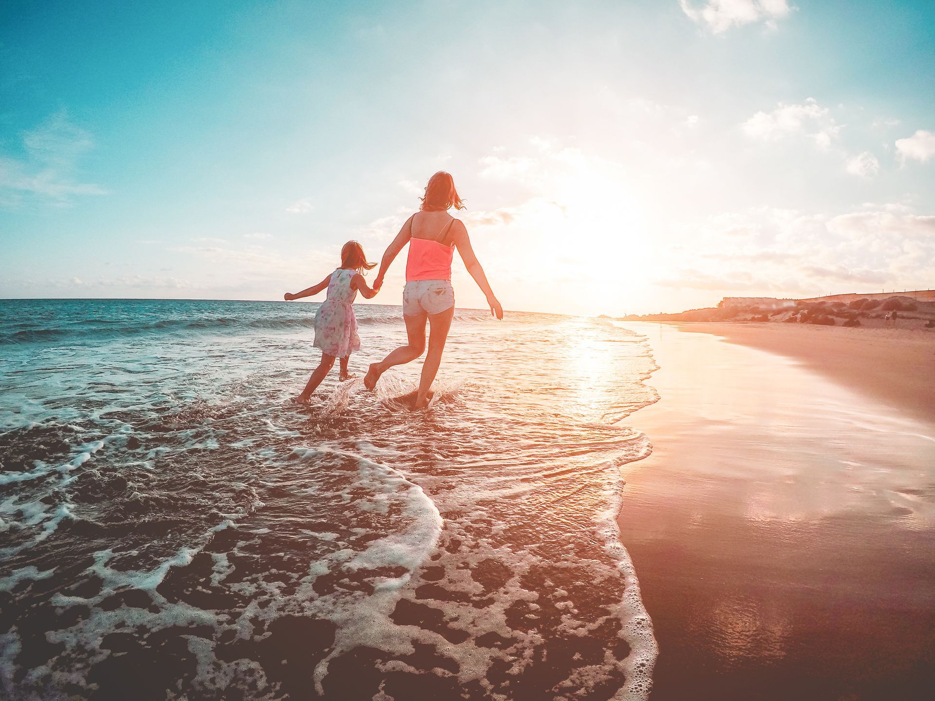 A woman and a child are running on the beach at sunset.