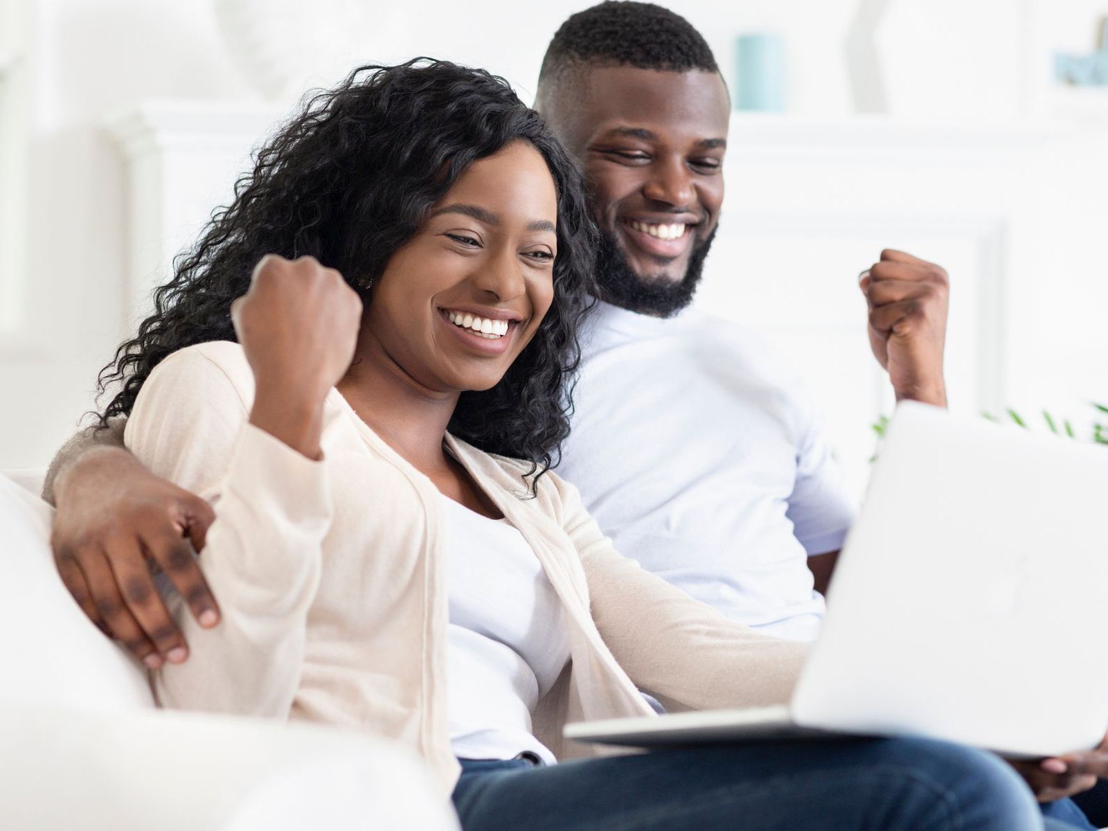 A man and a woman are sitting on a couch using a laptop computer.