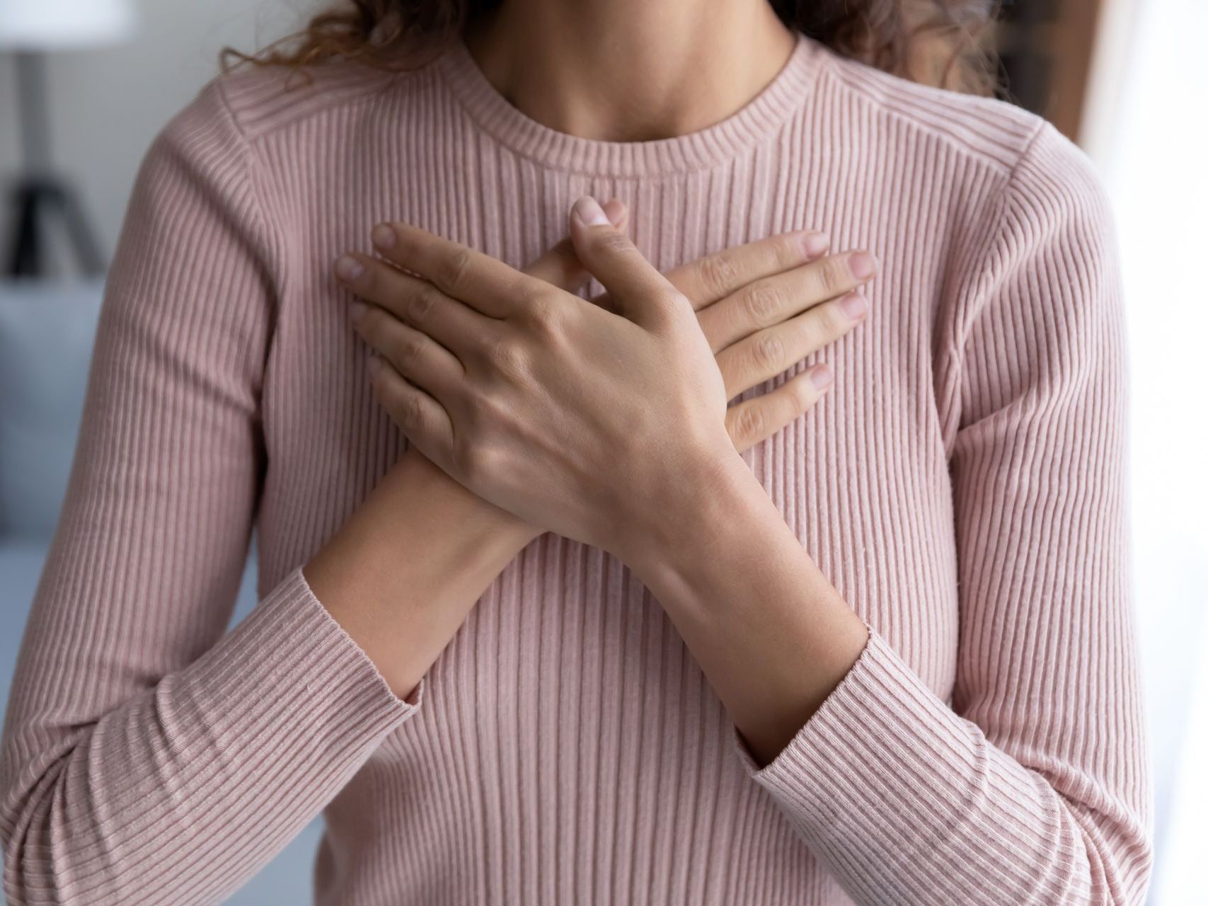 A woman in a pink sweater is holding her hands on her chest.