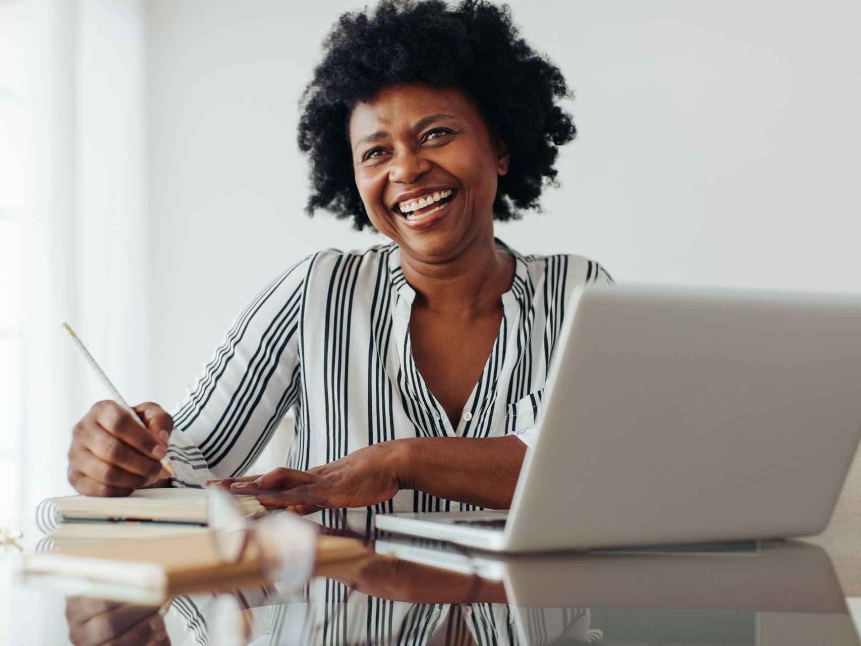 A woman is sitting at a desk with a laptop and a pen.
