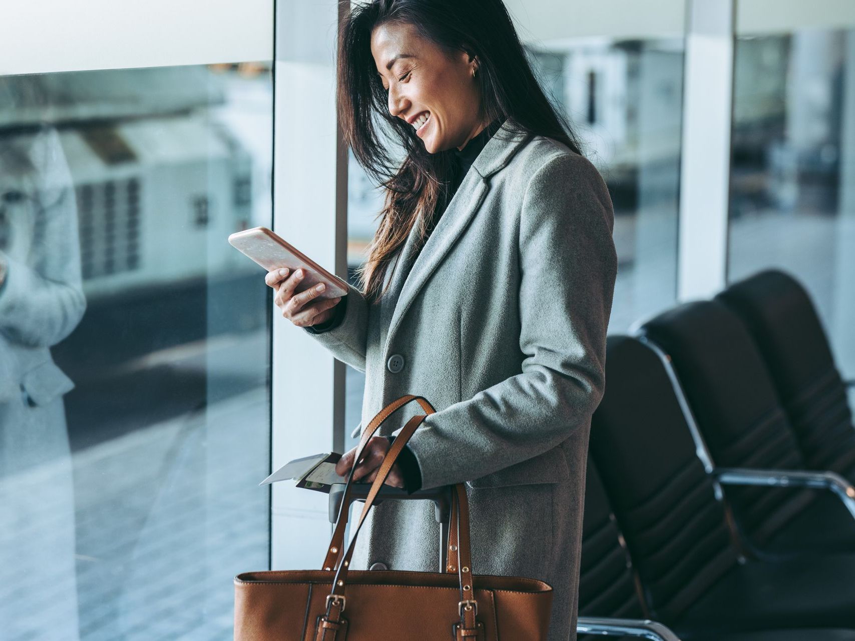 A woman is standing in an airport looking at her cell phone.