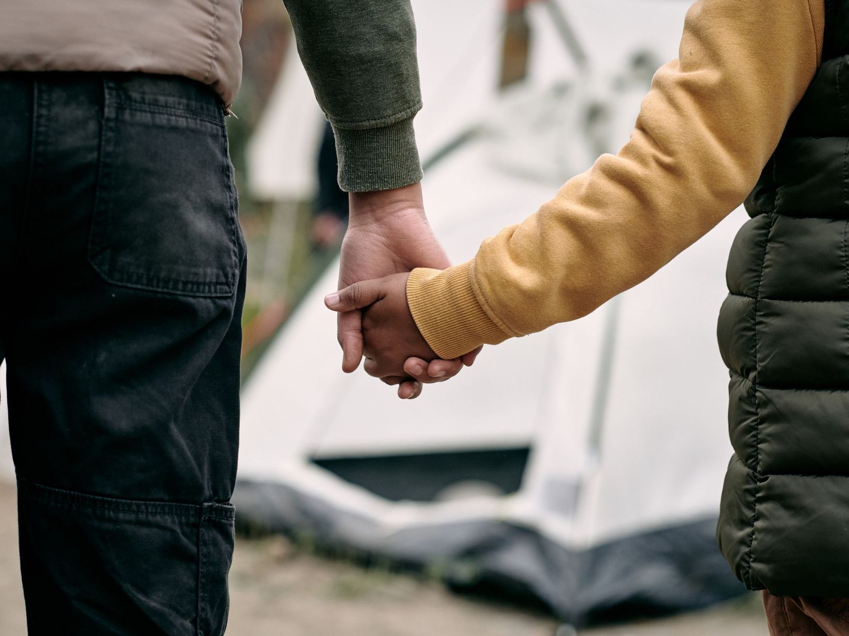 A man and a child are holding hands in front of a tent.