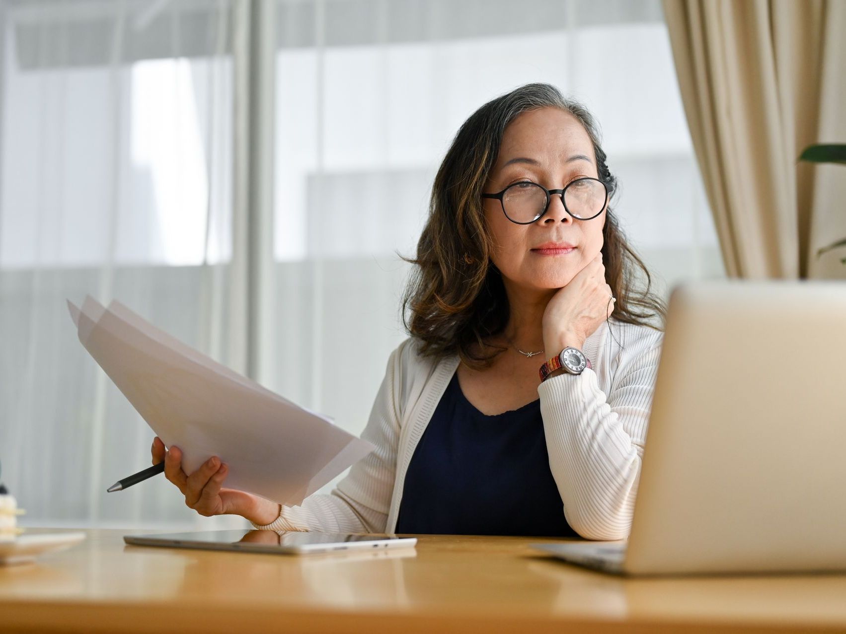 A woman is sitting at a desk holding a piece of paper and a pen.