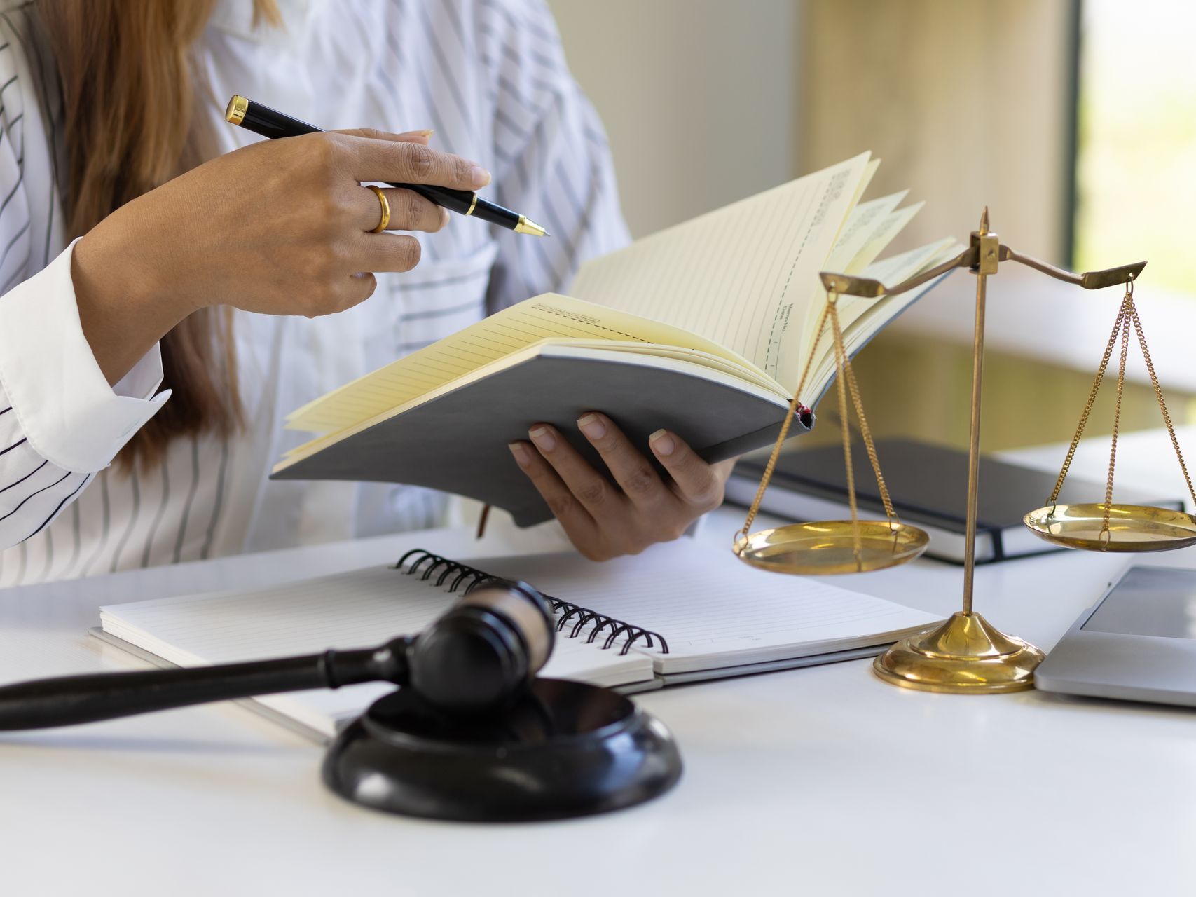 A woman is sitting at a desk holding a book and a pen.