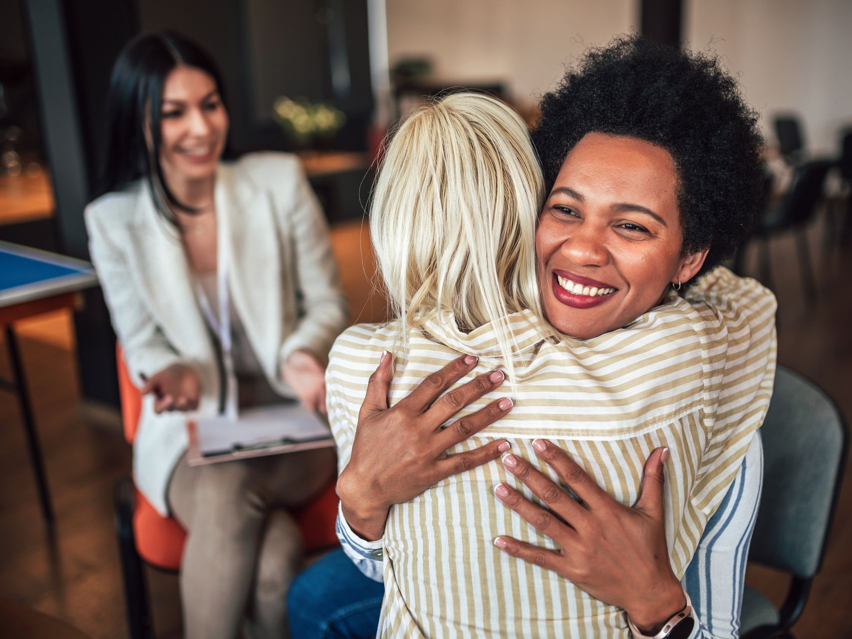 A woman is hugging another woman in a group therapy session.