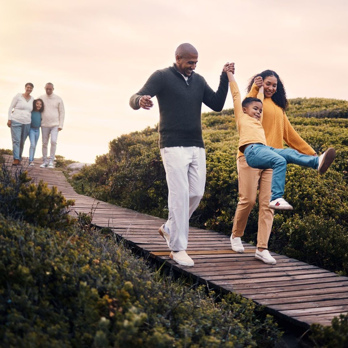 A family is walking down a wooden walkway holding hands.