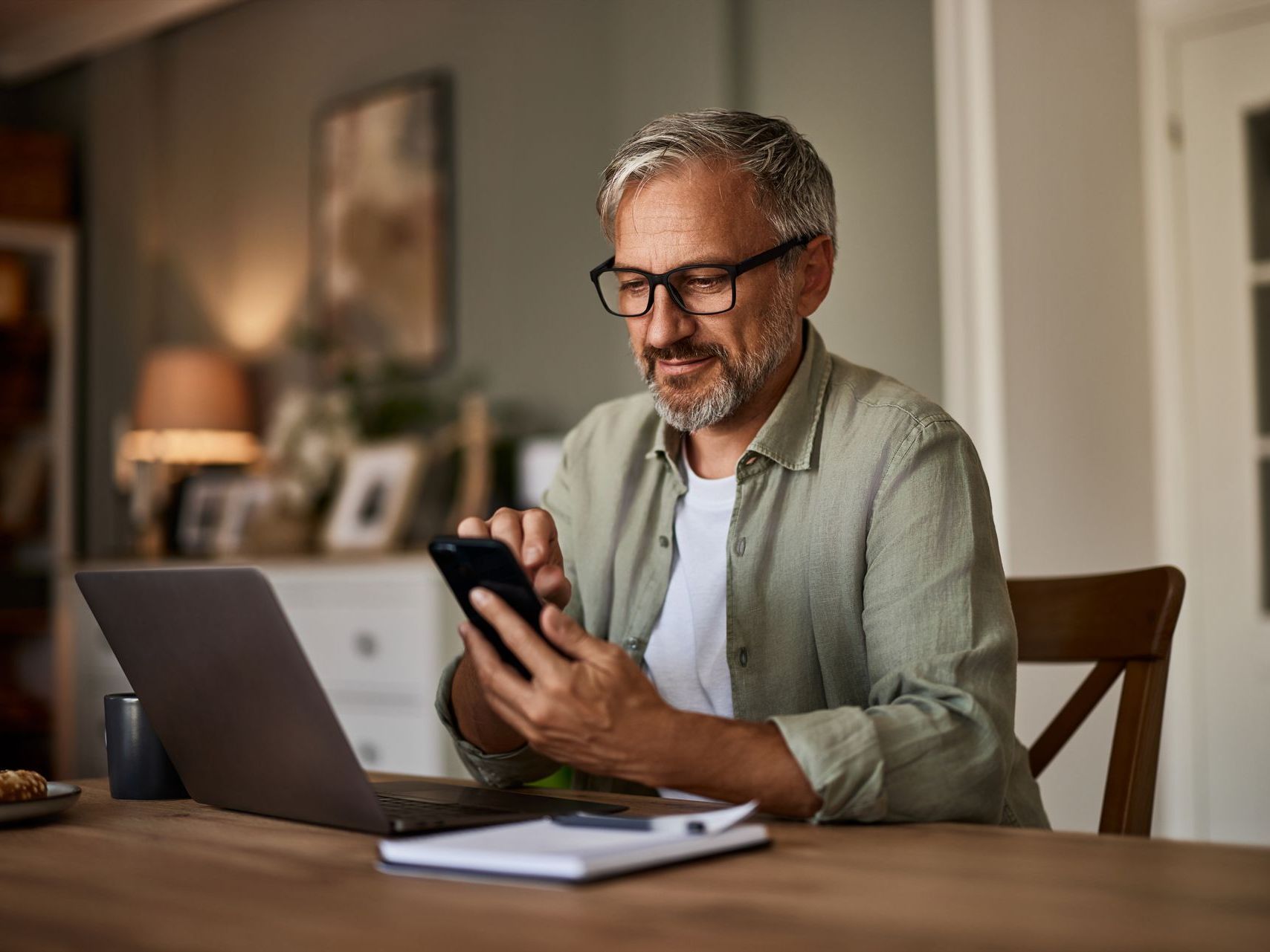 A man is sitting at a table using a laptop and a cell phone.
