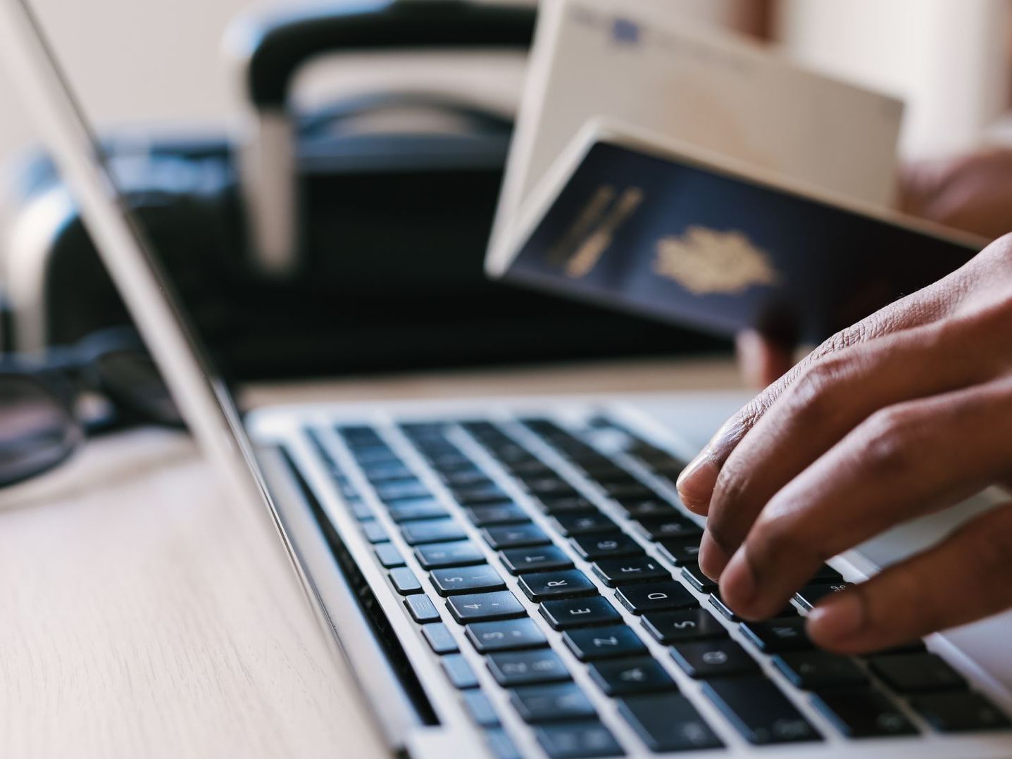A person is typing on a laptop with a passport in the background
