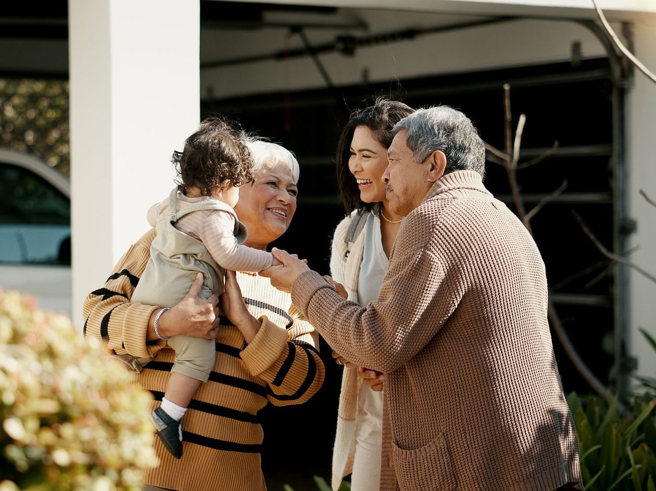 A group of people are standing outside of a house holding a baby.