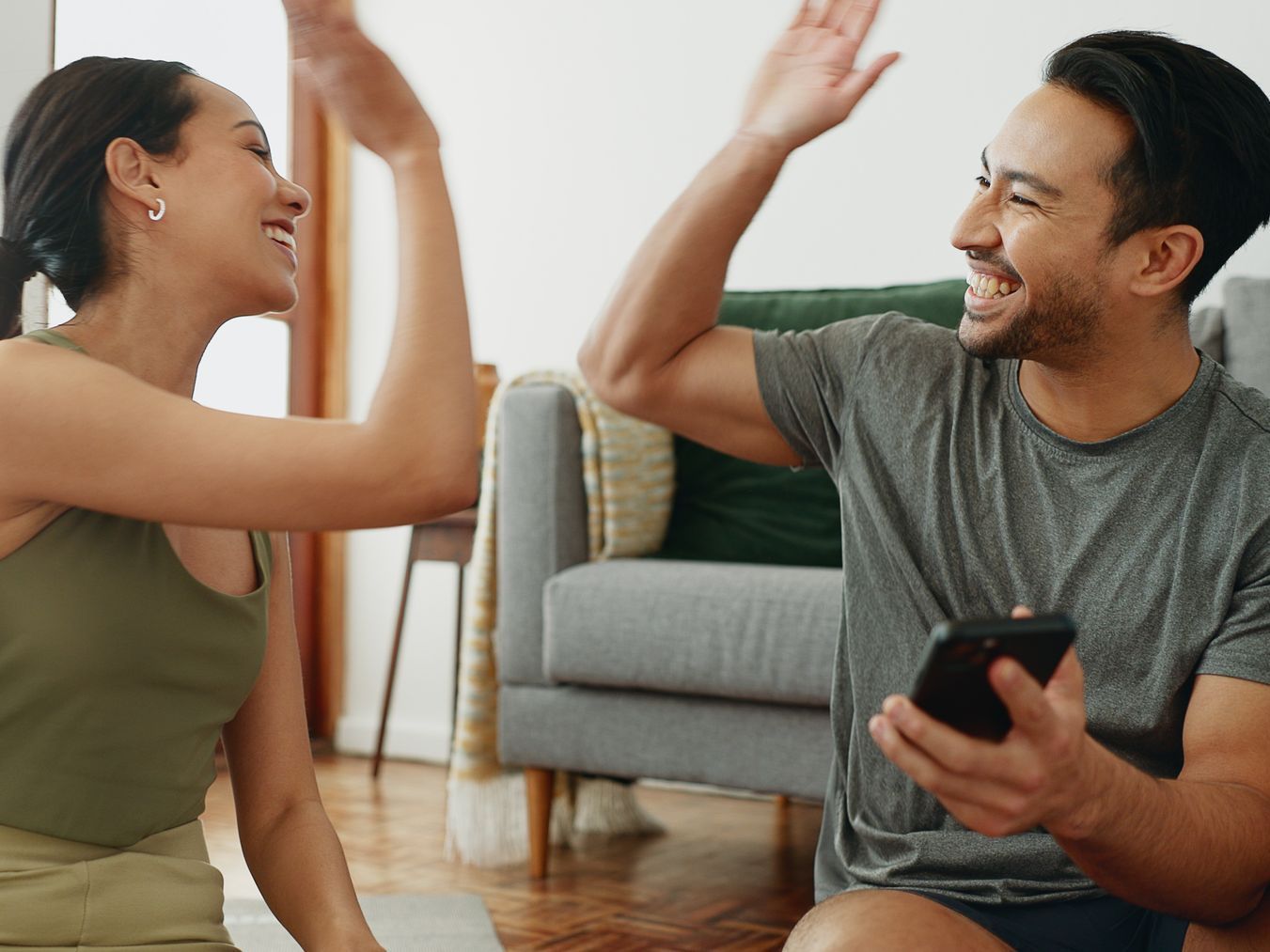A man and a woman are giving each other a high five while sitting on the floor.