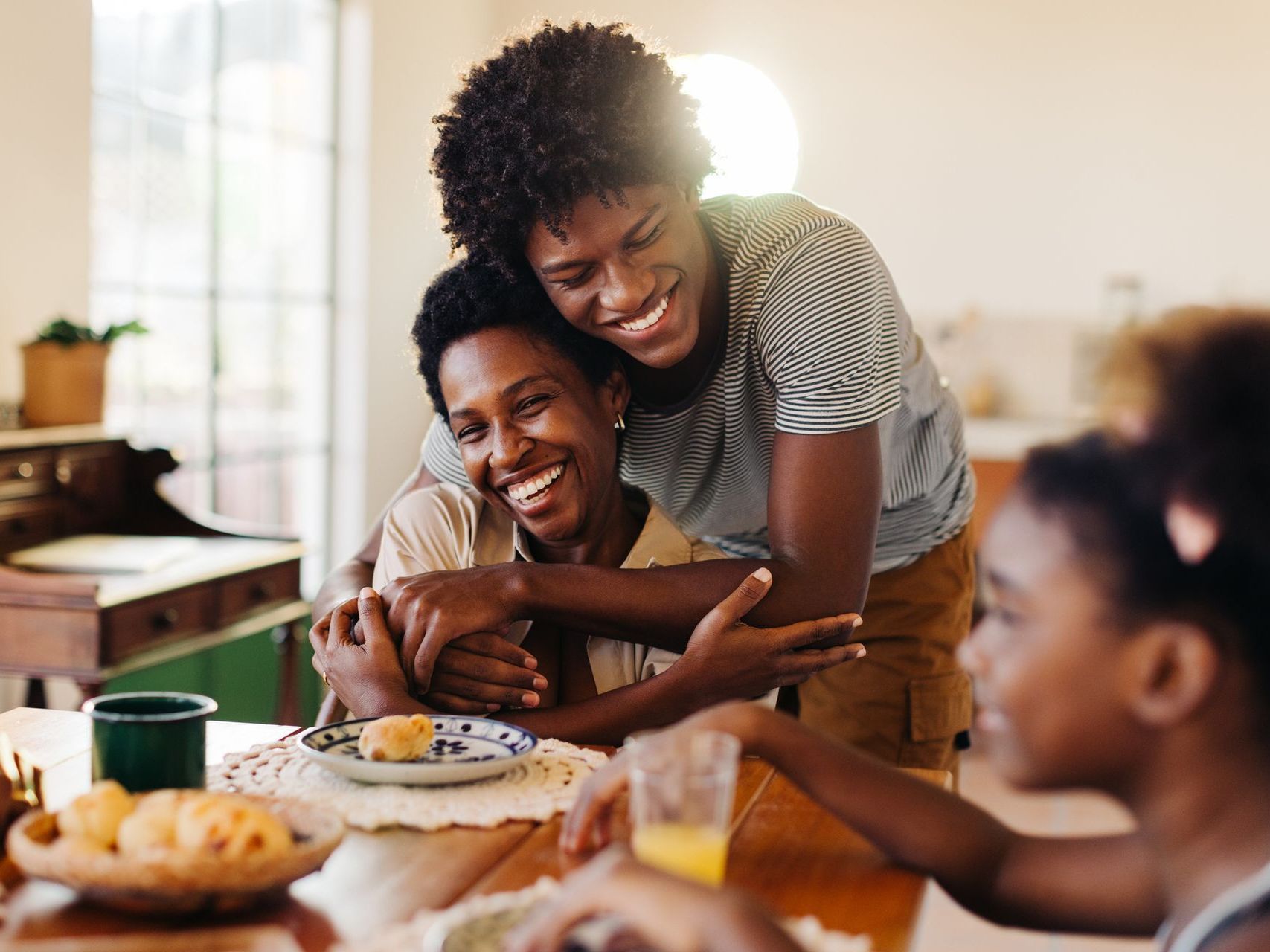 A family is sitting at a table hugging and smiling.