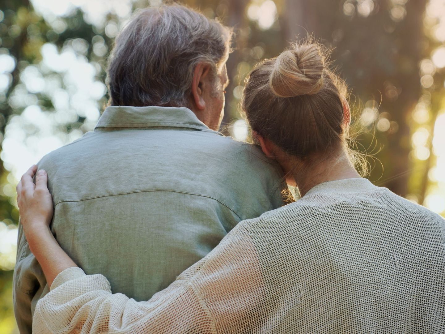 A woman is hugging an older man in a park.