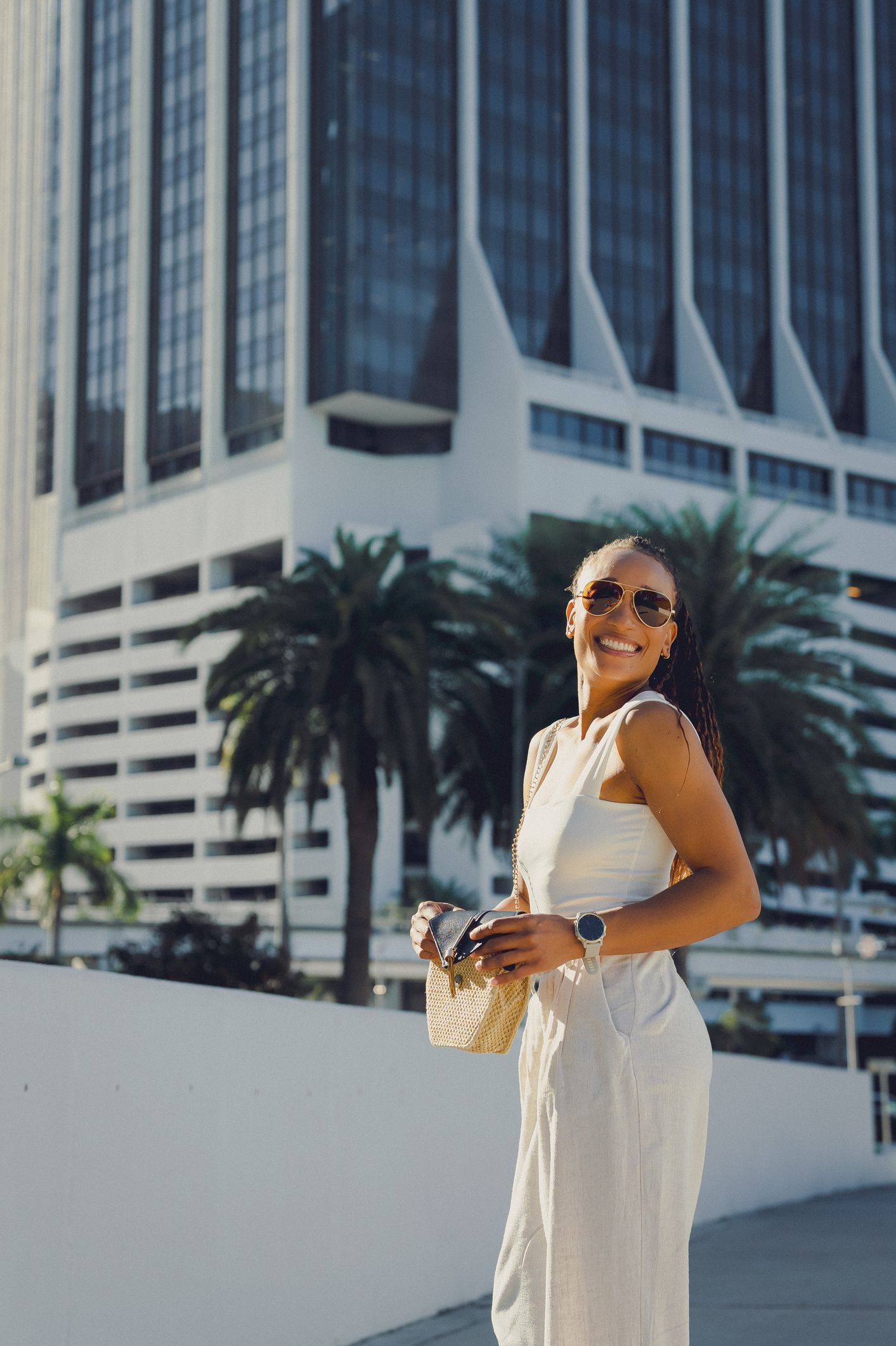 A woman in a white dress is standing in front of a tall building.