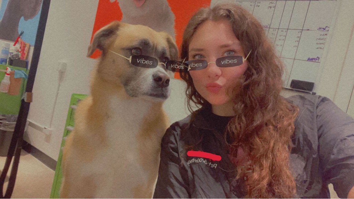 A woman is standing next to a dog wearing sunglasses.