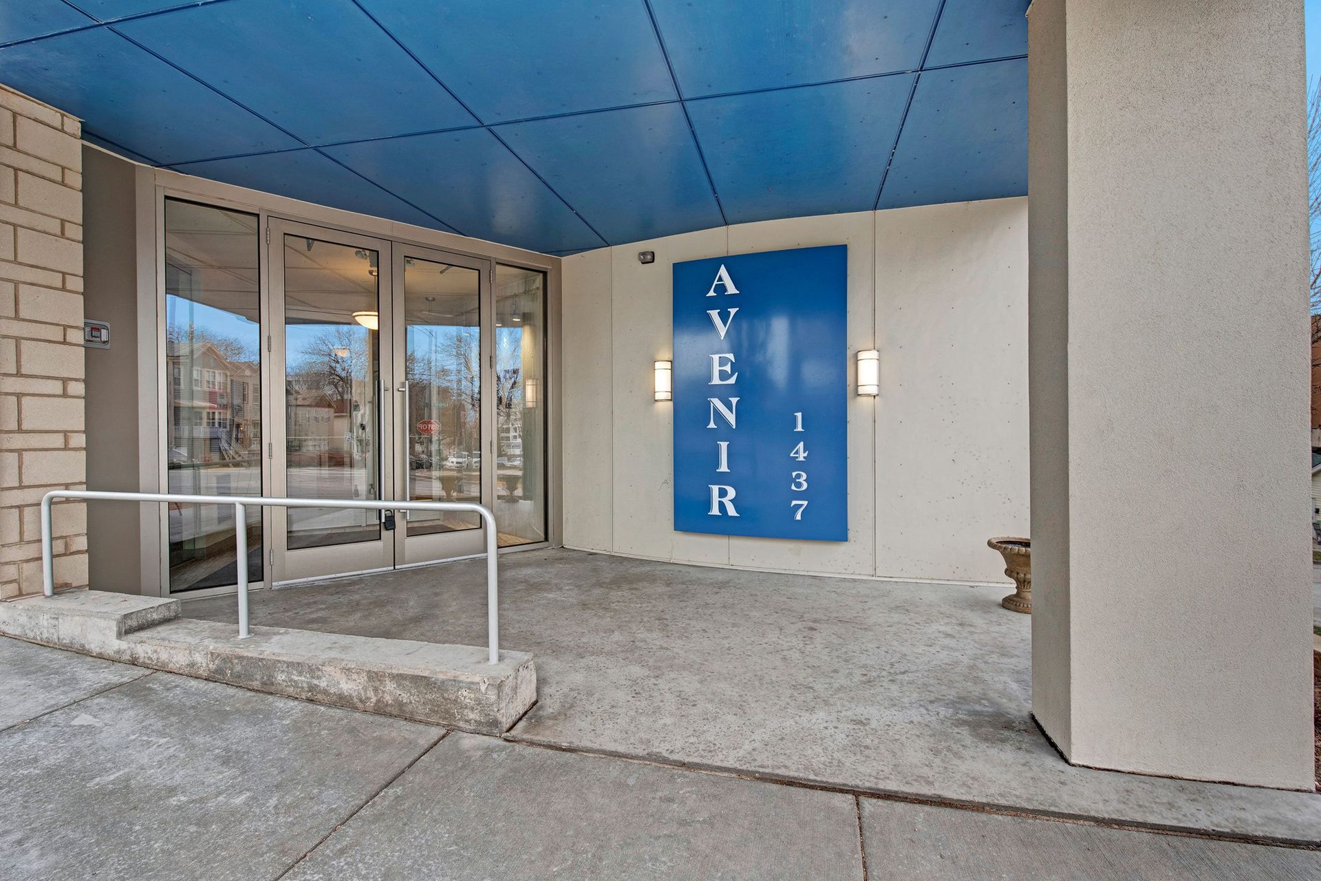 Entrance of Avenir Apartments with large glass doors and a blue sign reading 