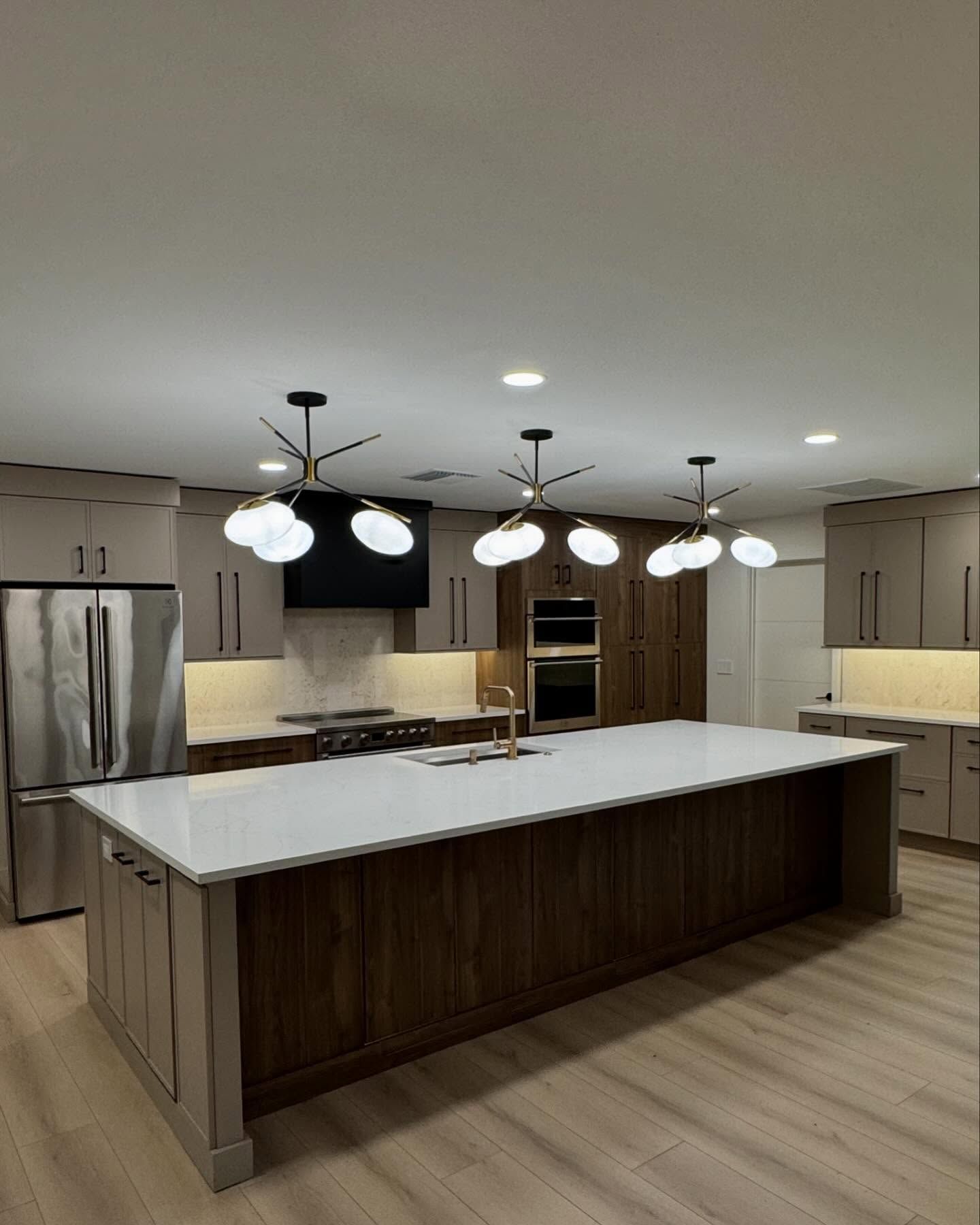 Modern kitchen with large island, white countertops, wood cabinets, stainless steel appliances, and pendant lights