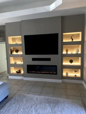 Modern living room wall with built-in shelves, a large TV, and a sleek fireplace on a gray accent wall.