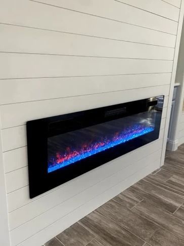 Modern electric fireplace with blue and pink flames set into a white shiplap wall indoors