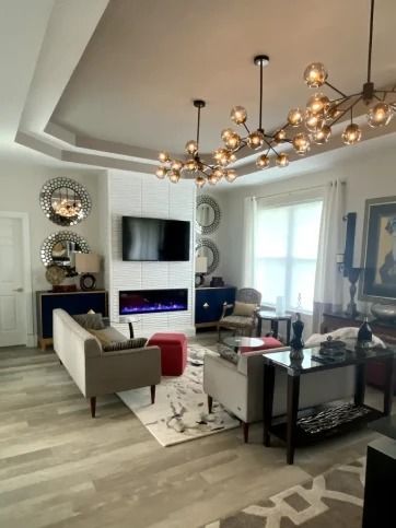 Stylish living room with beige sofa, glass table, fireplace TV, and gold chandelier.