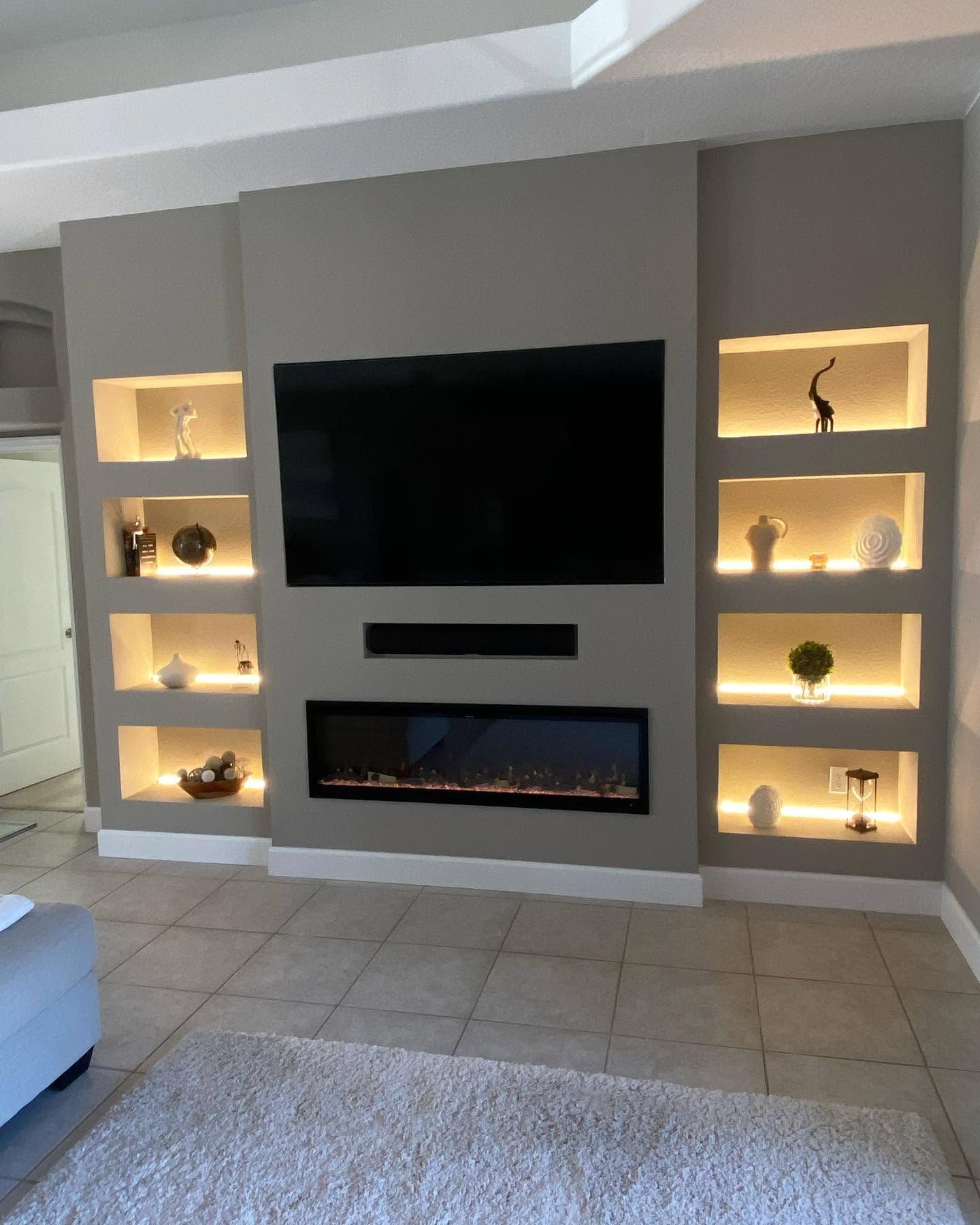 Built-in living room wall with TV, electric fireplace, and lit display shelves on both sides.