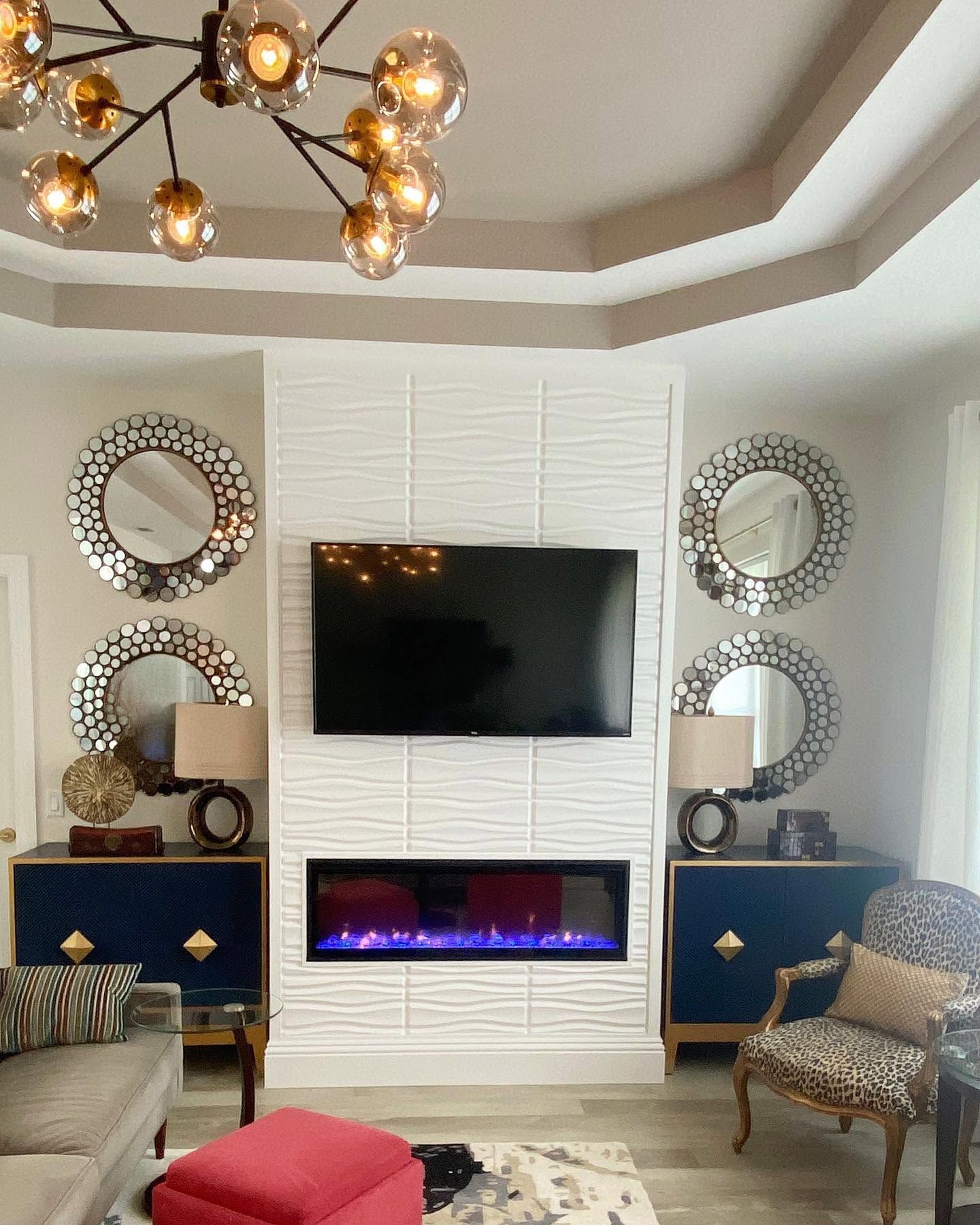 Modern living room with wall-mounted TV, electric fireplace, mirrored decor, and blue cabinets