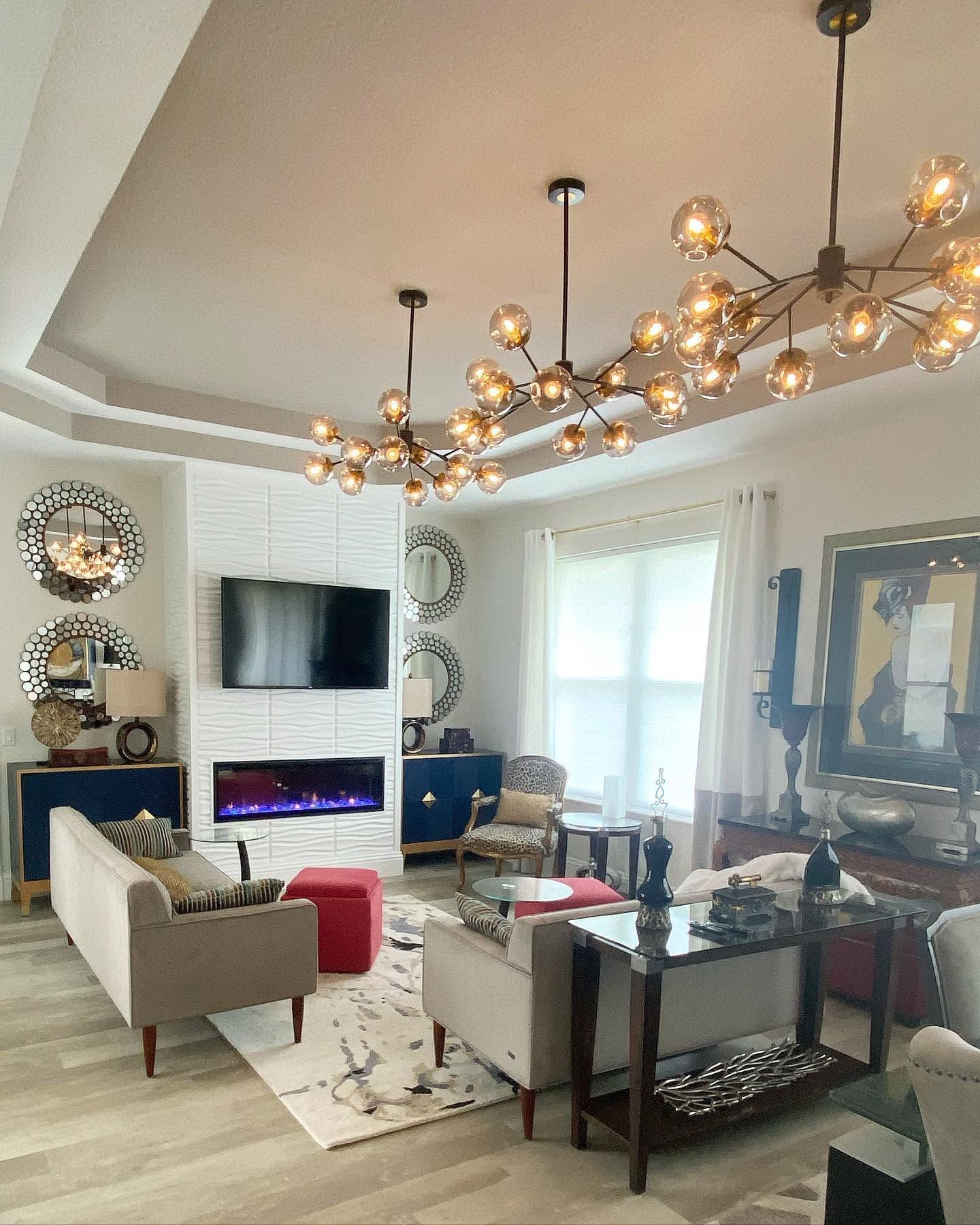 Modern living room with chandelier, wall-mounted TV, fireplace, and sofas around a coffee table.