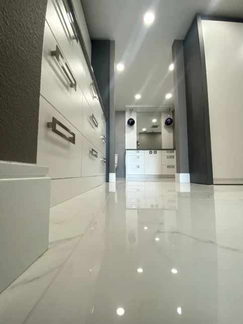 Bright modern hallway with glossy white tile floor, drawers on left, and recessed ceiling lights.