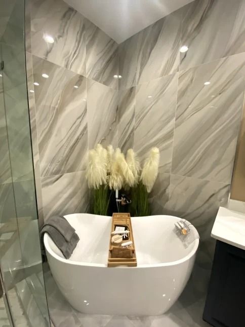 Modern bathroom with a white oval tub, marble walls, and a flower arrangement on a tray