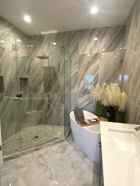Modern bathroom with glass shower, marble walls, and freestanding tub beside tall white flowers