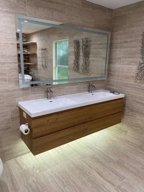 Modern bathroom vanity with wood cabinet, large mirror, and under-cabinet lighting.
