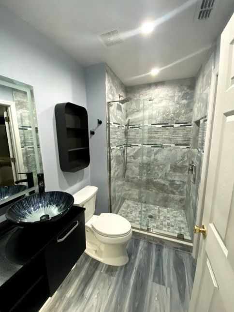 Modern bathroom with black vanity, vessel sink, toilet, and glass shower with gray marble tile
