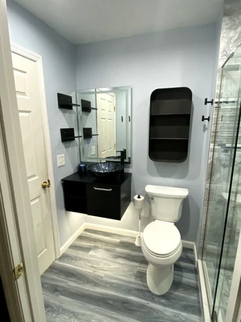 Small bathroom with gray walls, vanity sink, toilet, shower, and wood-look floor tiles