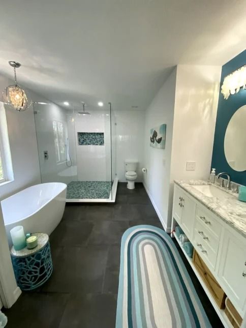 Bright modern bathroom with freestanding tub, walk-in shower, dark floor, and blue striped rug