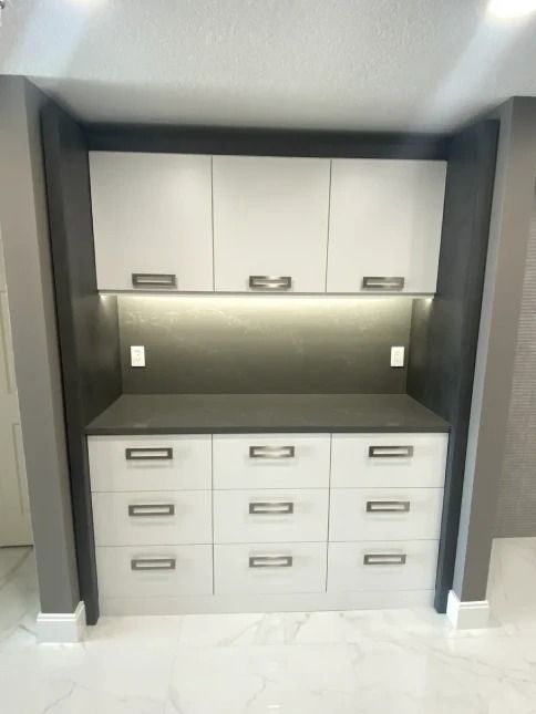 Built-in gray desk nook with upper cabinets, drawers, and under-cabinet lighting.