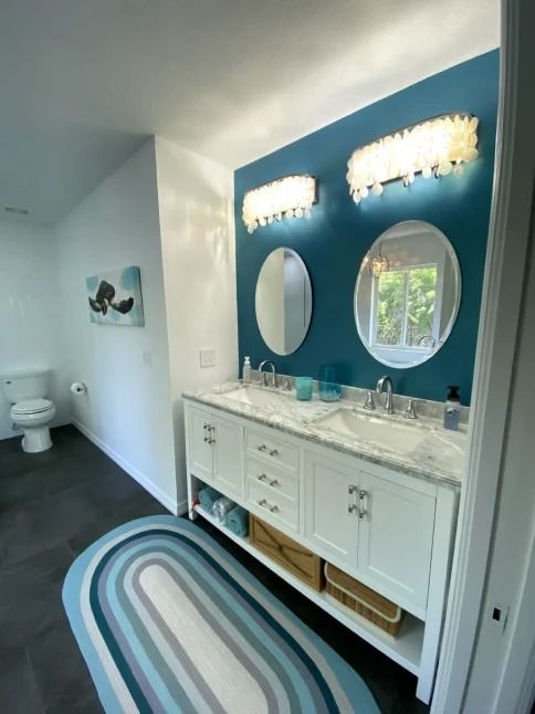 Bright bathroom vanity with marble countertop, round mirrors, blue accent wall, and striped rug