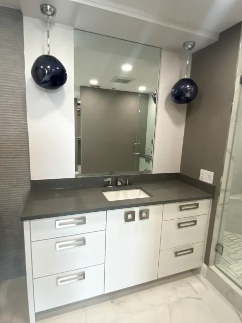 Modern bathroom vanity with mirror, gray countertop, white cabinets, and dark spherical wall lights