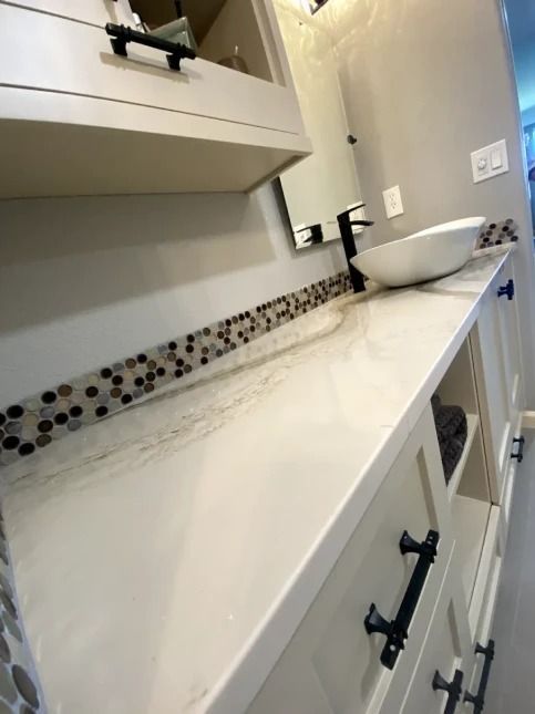 Bathroom vanity with white countertop, mosaic backsplash, sink, and black cabinet hardware