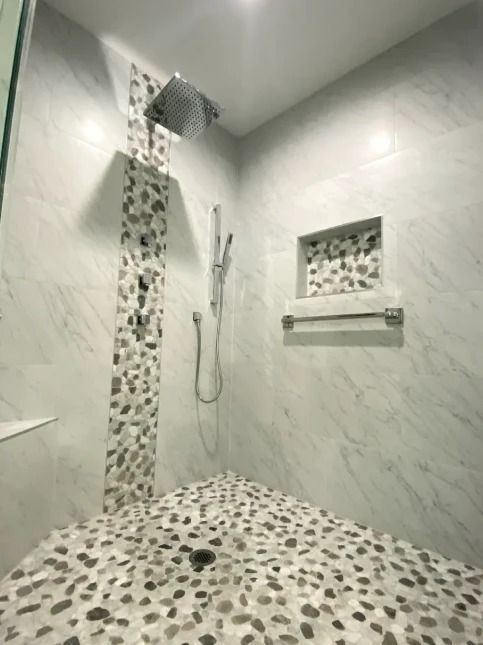 Modern shower with pebble tile floor, marble walls, rain showerhead, handheld shower, and wall niche.