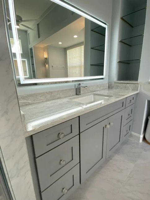 Modern bathroom vanity with light gray cabinets, marble countertop, and illuminated mirror