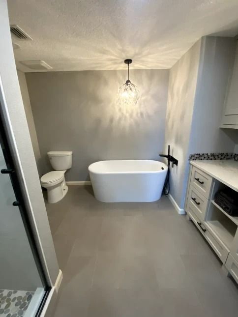 Modern bathroom with freestanding tub, toilet, walk-in shower, and vanity with marble countertop.