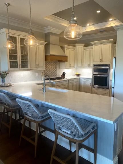 Bright modern kitchen with white cabinets, marble island, pendant lights, and woven bar stools.