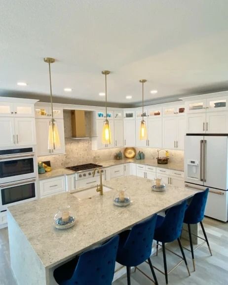 Bright modern white kitchen with granite island, blue barstools, pendant lights, and stainless steel appliances
