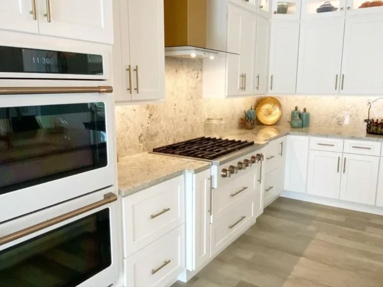 Bright white kitchen with double wall ovens, gas range, marble backsplash, and light wood flooring