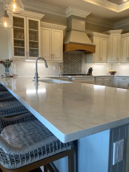 Modern kitchen with white cabinets, large marble island, and barstools under warm lighting